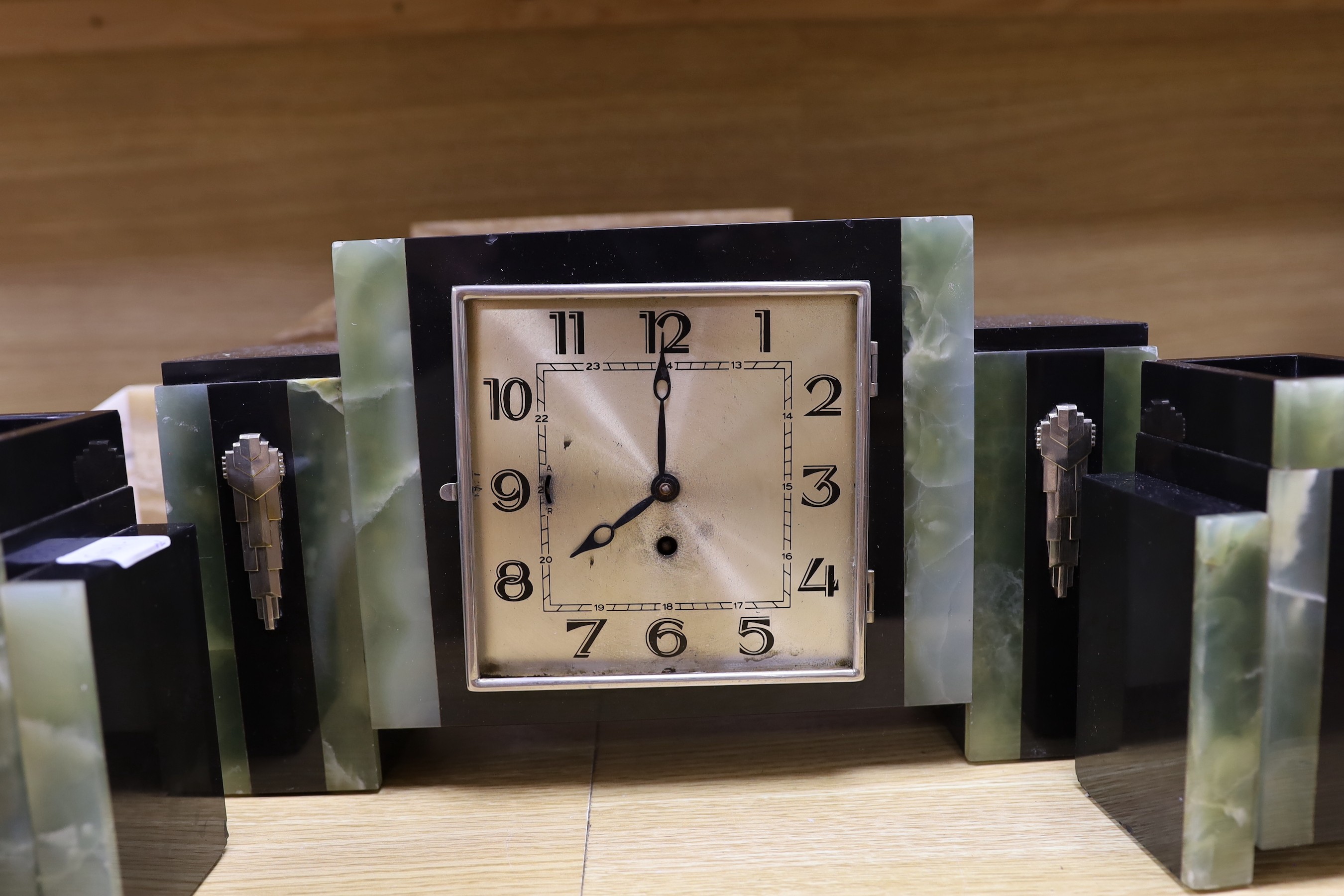 An Art Deco marble and onyx clock garniture, together with another stylised onyx Art Deco marble clock garniture with decorative silver-coloured reliefs